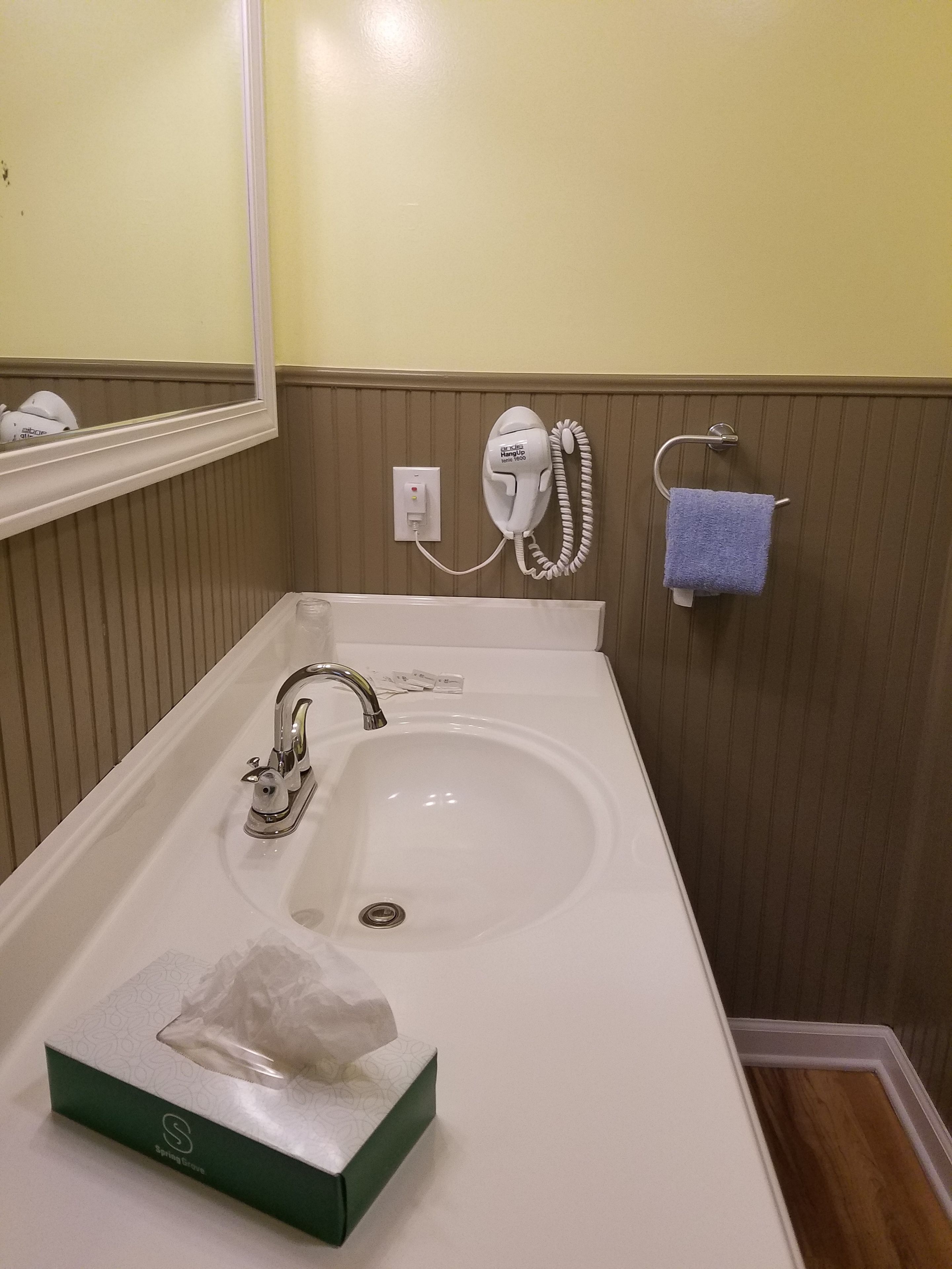 Un baño con lavamanos blanco, un espejo, un teléfono y un perchero para toallas.