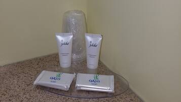 A bathroom counter with toiletries including two bottles of jade conditioning shampoo, a bottle of jade conditioner, and two packets of Oasis soap.