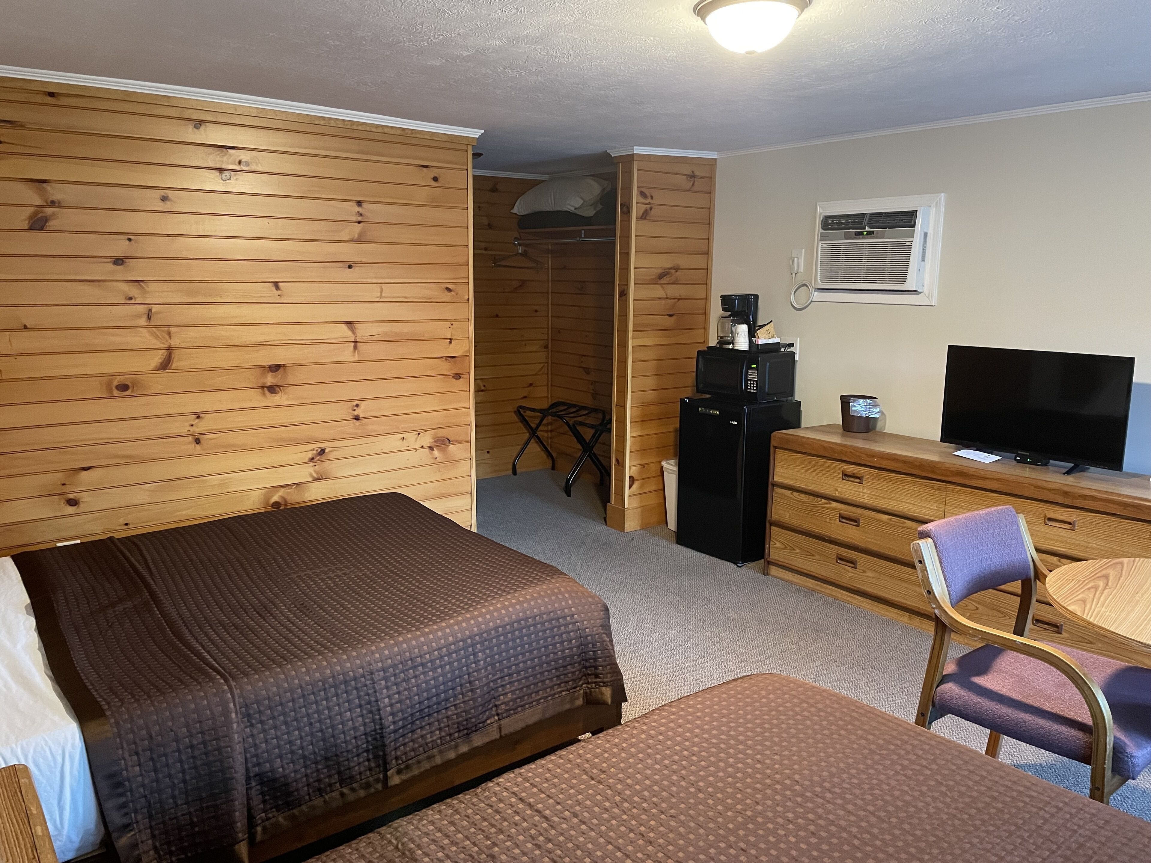 A hotel room with two beds, a desk, a chair, a television, a refrigerator, and a microwave.