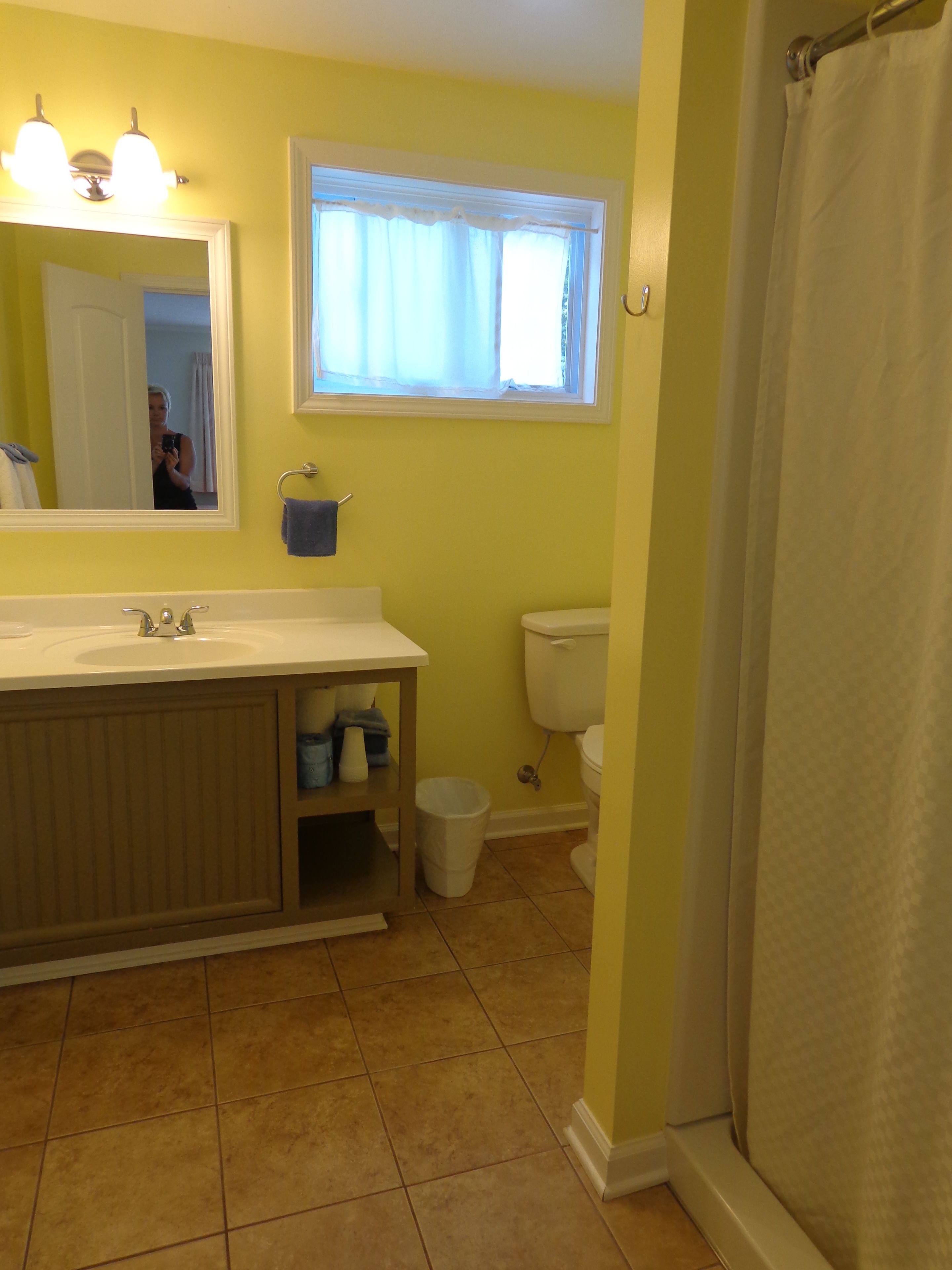 Baño con lavamanos, espejo, ventana, inodoro y cortina de ducha.