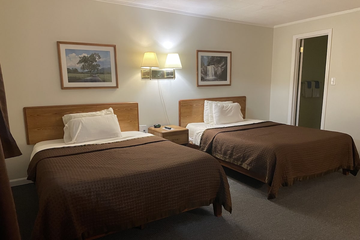 A hotel room with two beds, a nightstand, wall-mounted lamps, and framed pictures on the walls.