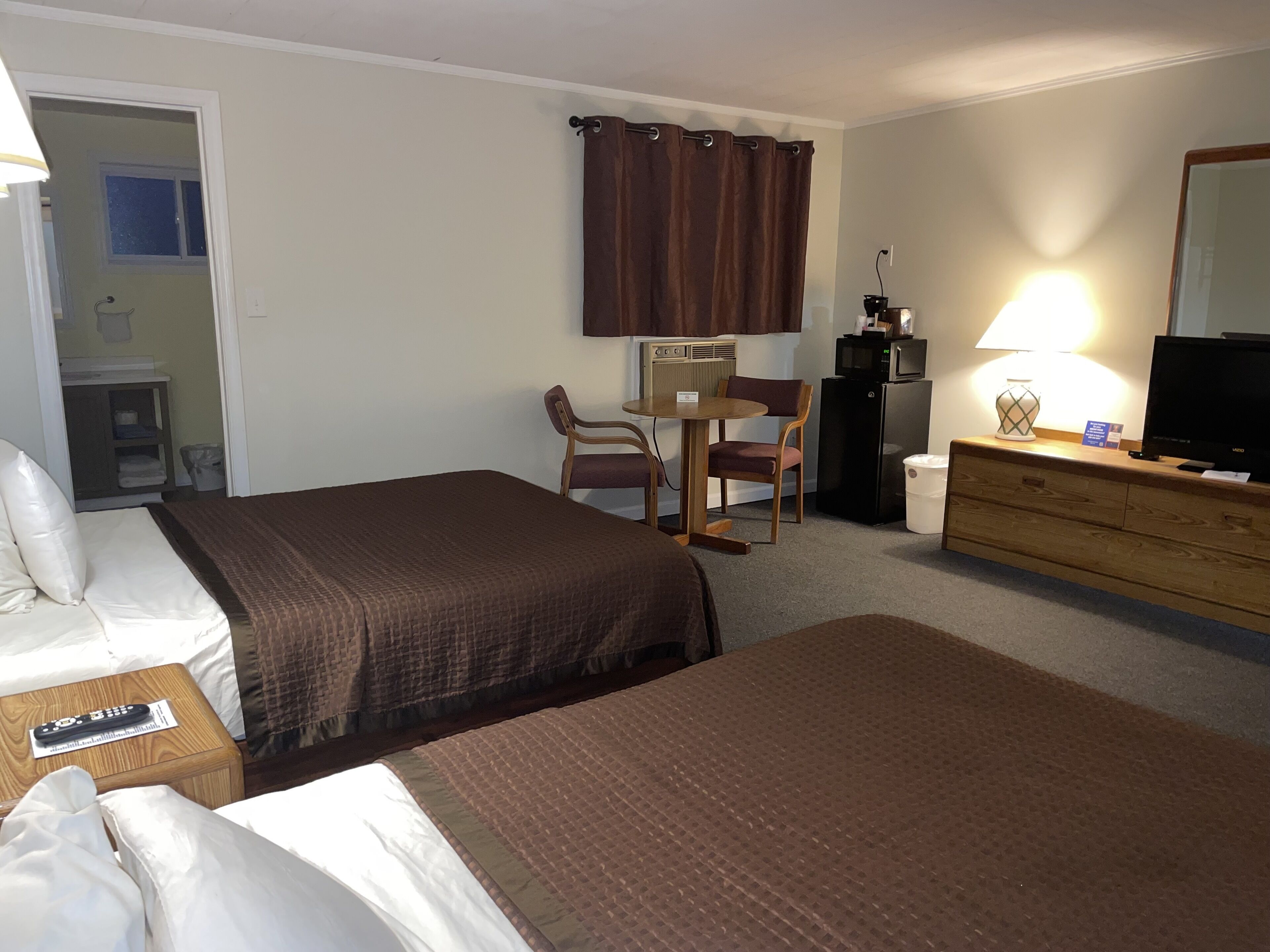 A hotel room with two beds, a desk, a chair, a television, a dresser, and a mirror.