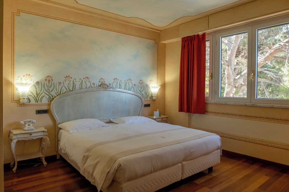 A hotel room with a large bed, a nightstand with a telephone, and a window with curtains.