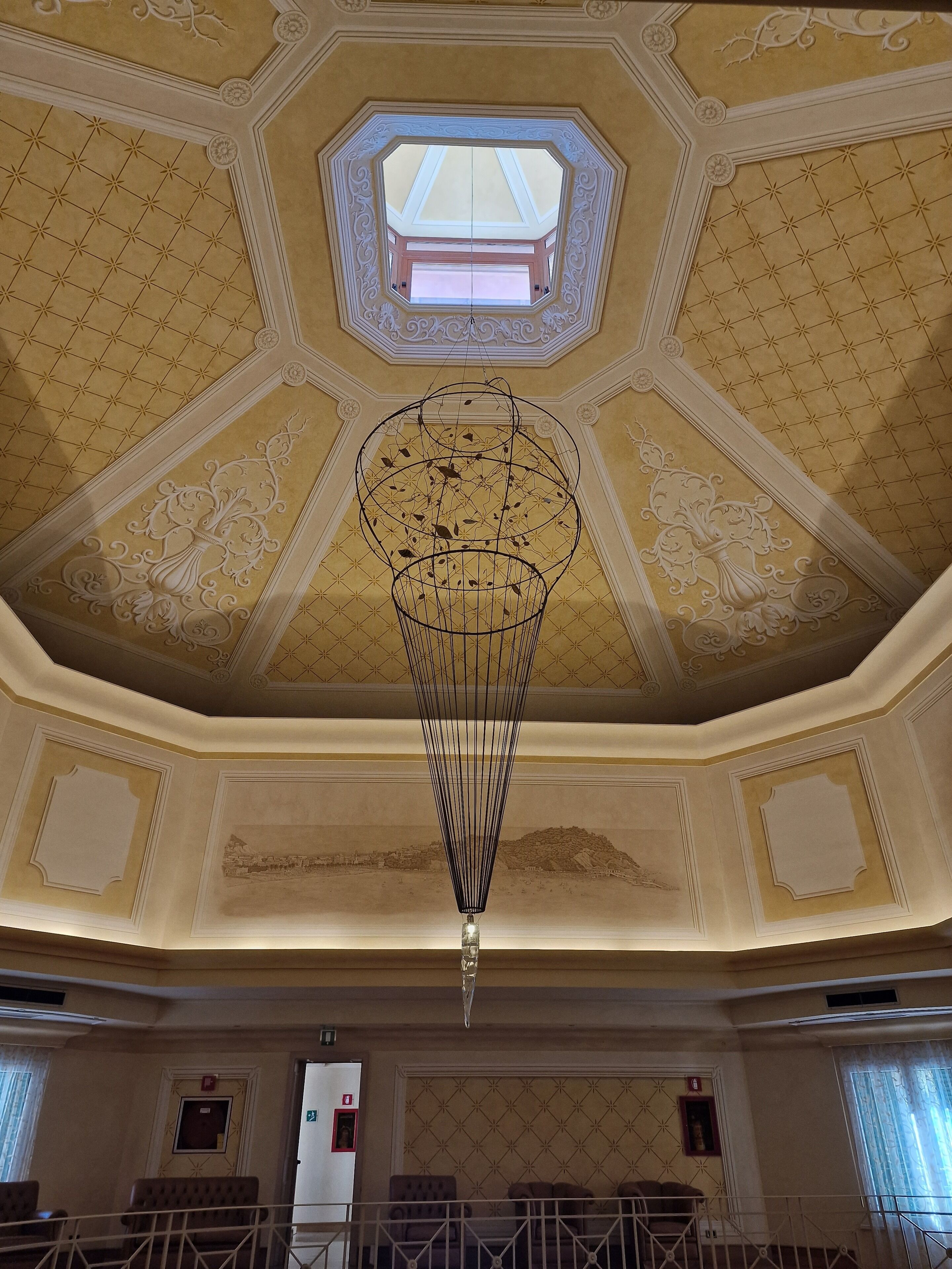 A grand hall with a high, ornate ceiling featuring a central chandelier and a skylight.