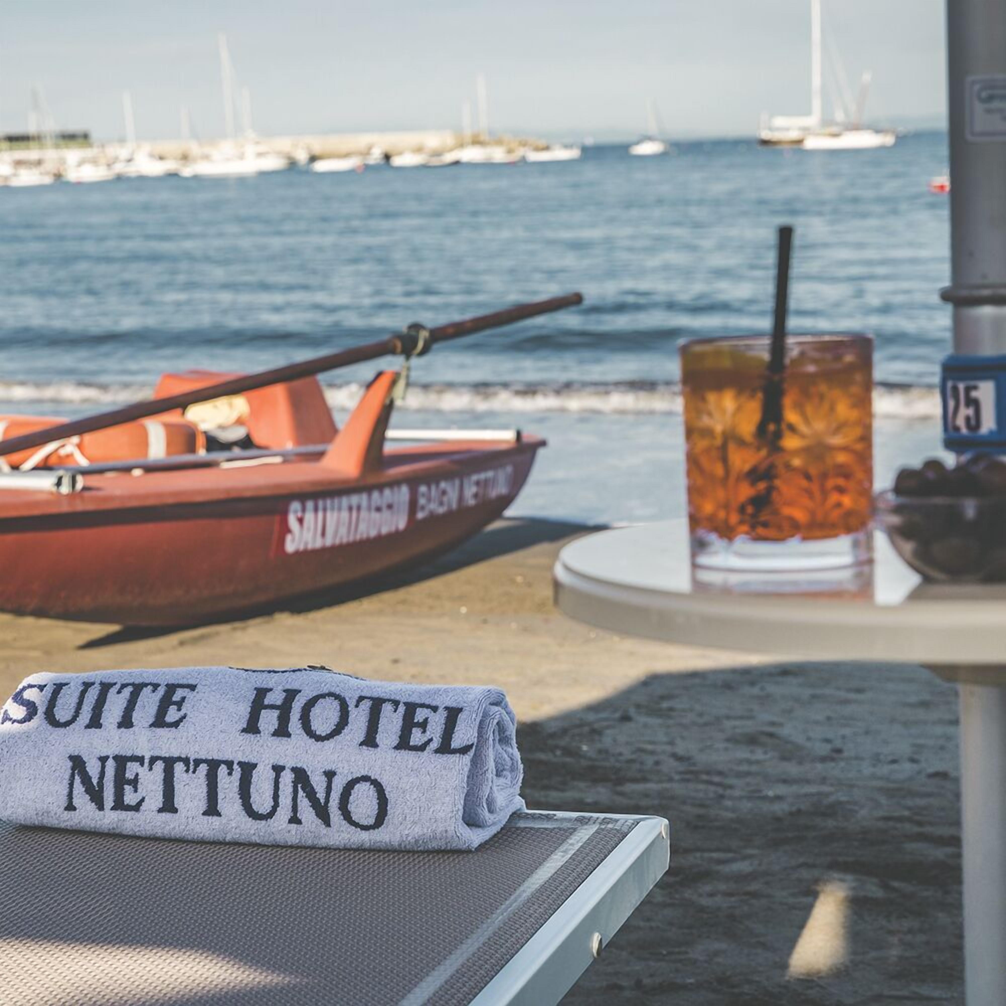 A beach scene with a rowboat, a drink, and a towel with "SUITE HOTEL NETTUNO" text.
