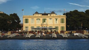 A waterfront building with a balcony overlooking the water, surrounded by outdoor seating areas.
