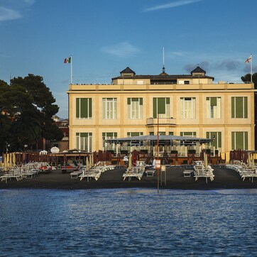 A waterfront building with a balcony overlooking the water, surrounded by outdoor seating areas.