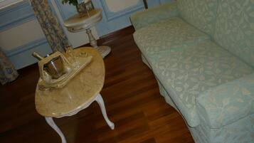 A room with a patterned sofa, a small round table with a tray holding a champagne bottle and glasses, a vase with flowers, and a patterned wall.