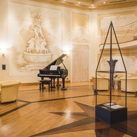 Een statig atrium met een vleugelpiano, een sculptuur en een trap.