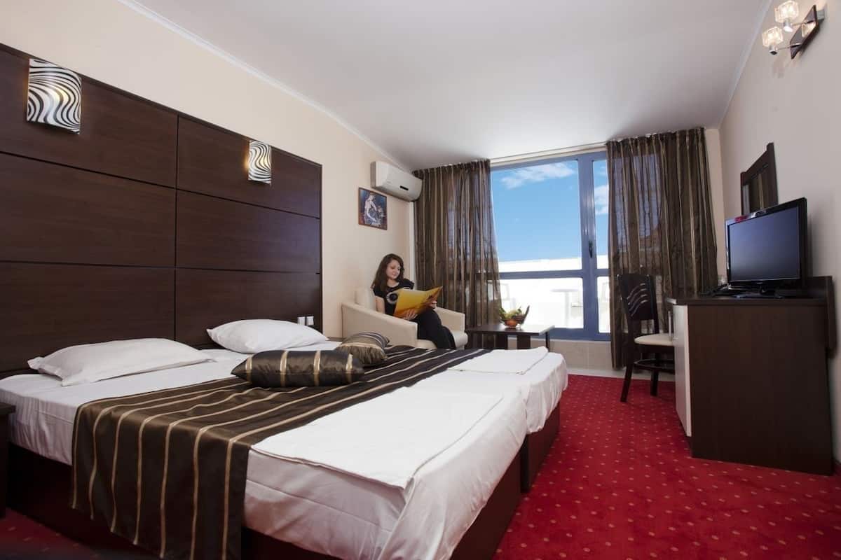 A hotel room with two beds, a desk, a television, and a window with curtains.