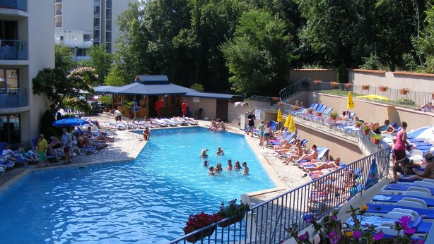 A swimming pool surrounded by lounge chairs and umbrellas, with people swimming and relaxing. - Hotel Royal (Golden Sands)