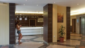A reception area with a reception desk, a clock, and a potted plant. - Hotel Royal (Golden Sands)