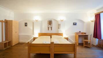 A wooden bed with two pillows, a wooden desk, and a bench in a room with white walls and wooden flooring.