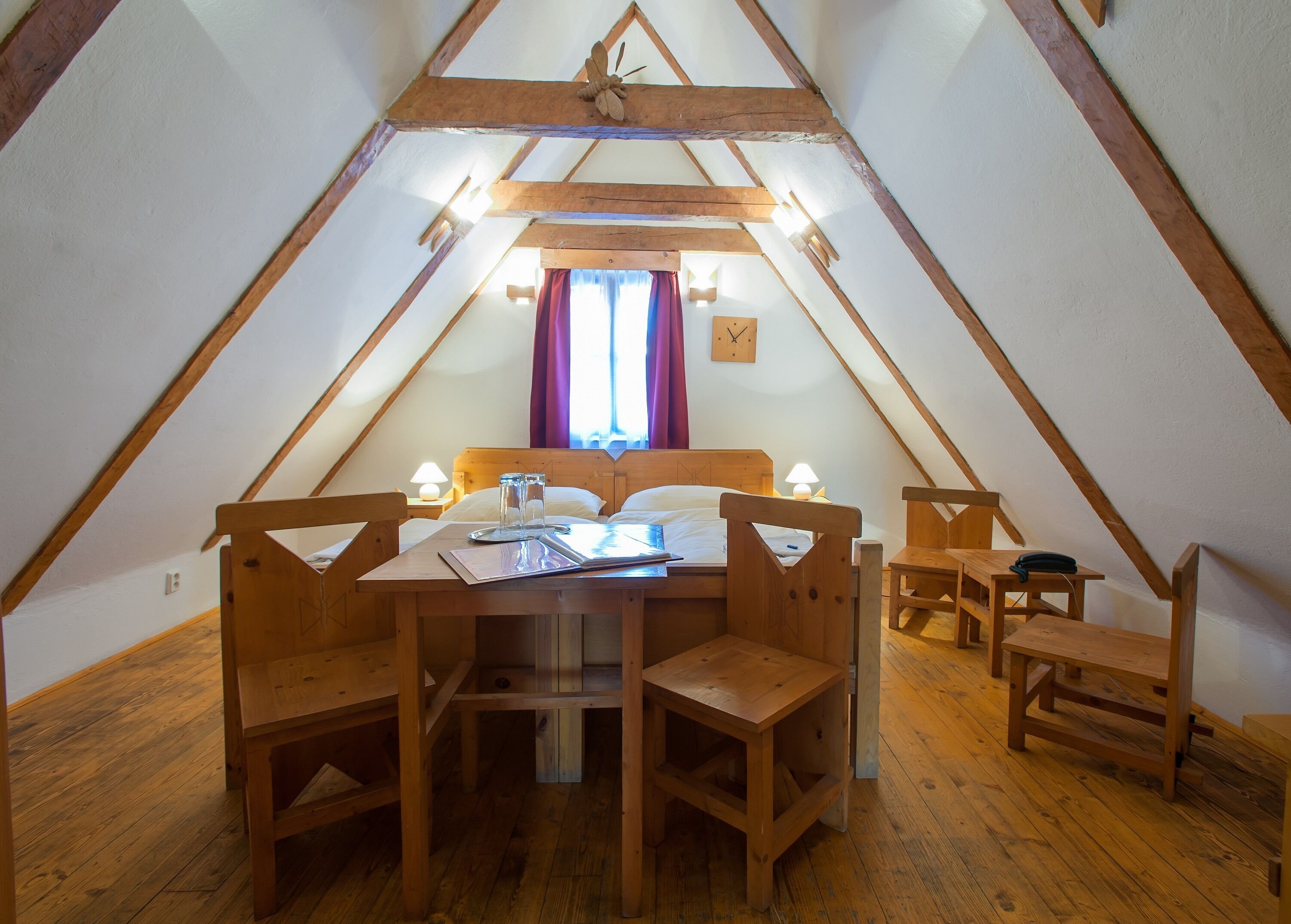 Un dormitorio acogedor en el ático, con una mesa de madera, dos sillas, una cama y un taburete pequeño de madera.
