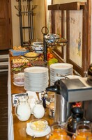 Una mesa de buffet con diversos alimentos, platos y una máquina de café.