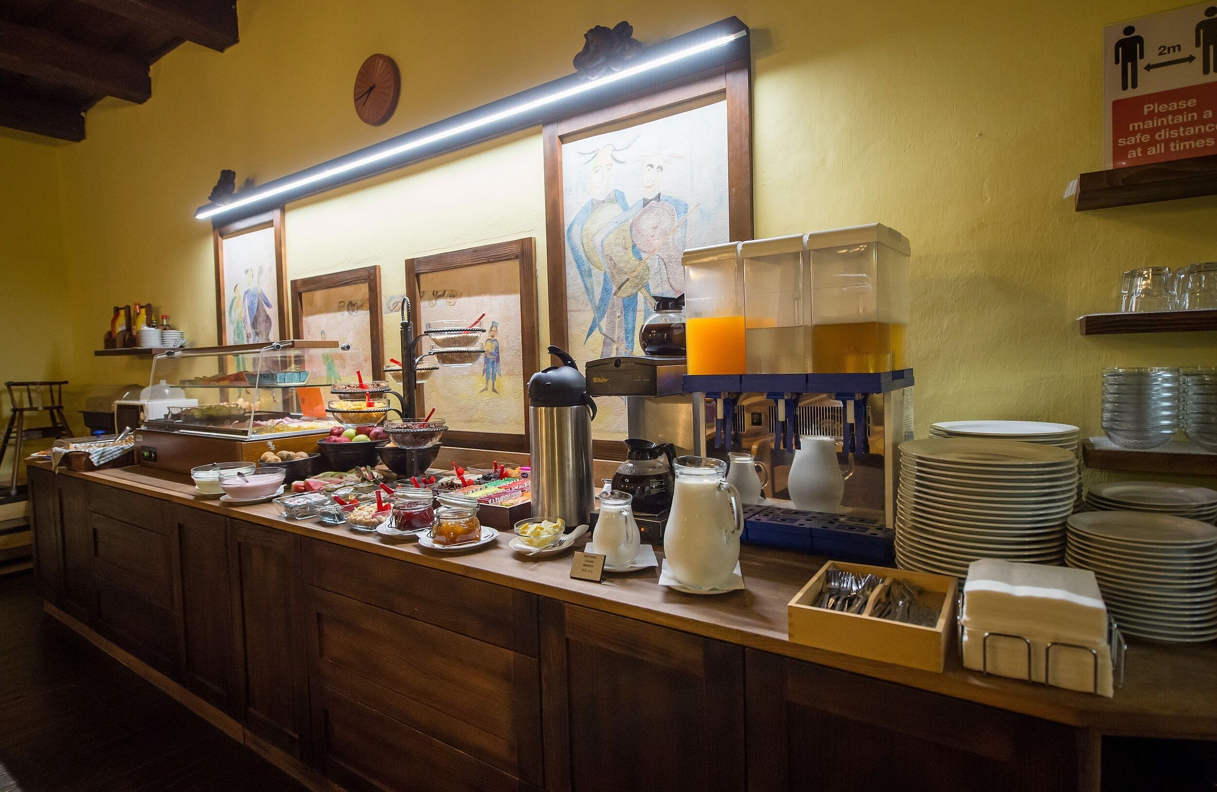Un buffet proposant divers plats, un espace dédié au café et un panneau indiquant les consignes de distanciation sociale, soit une distance de 2 mètres.