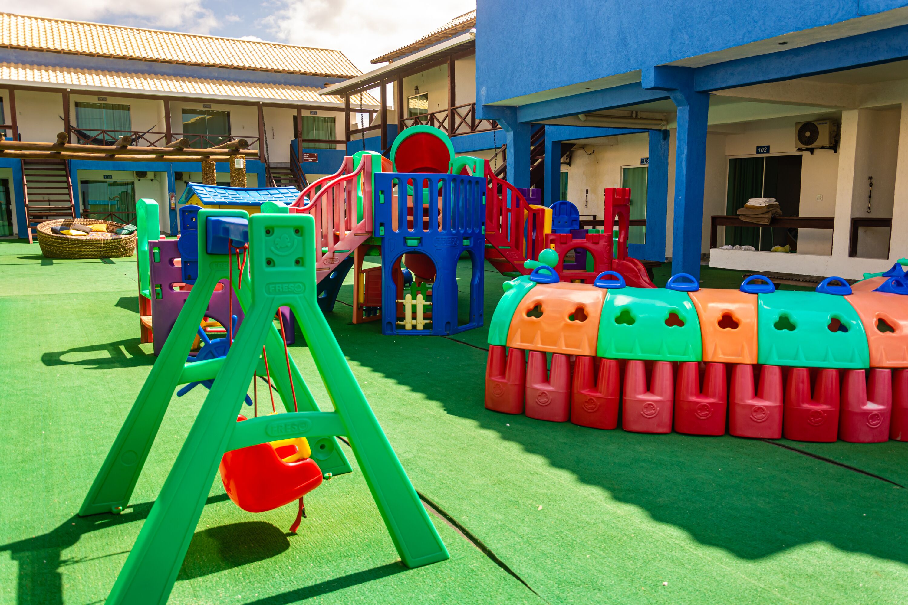Un'area giochi per bambini con diverse strutture colorate, tra cui uno scivolo e strutture per arrampicarsi, di fronte a un edificio con molte finestre e porte.