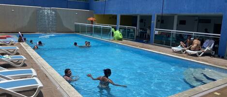A swimming pool with lounge chairs and a water slide.