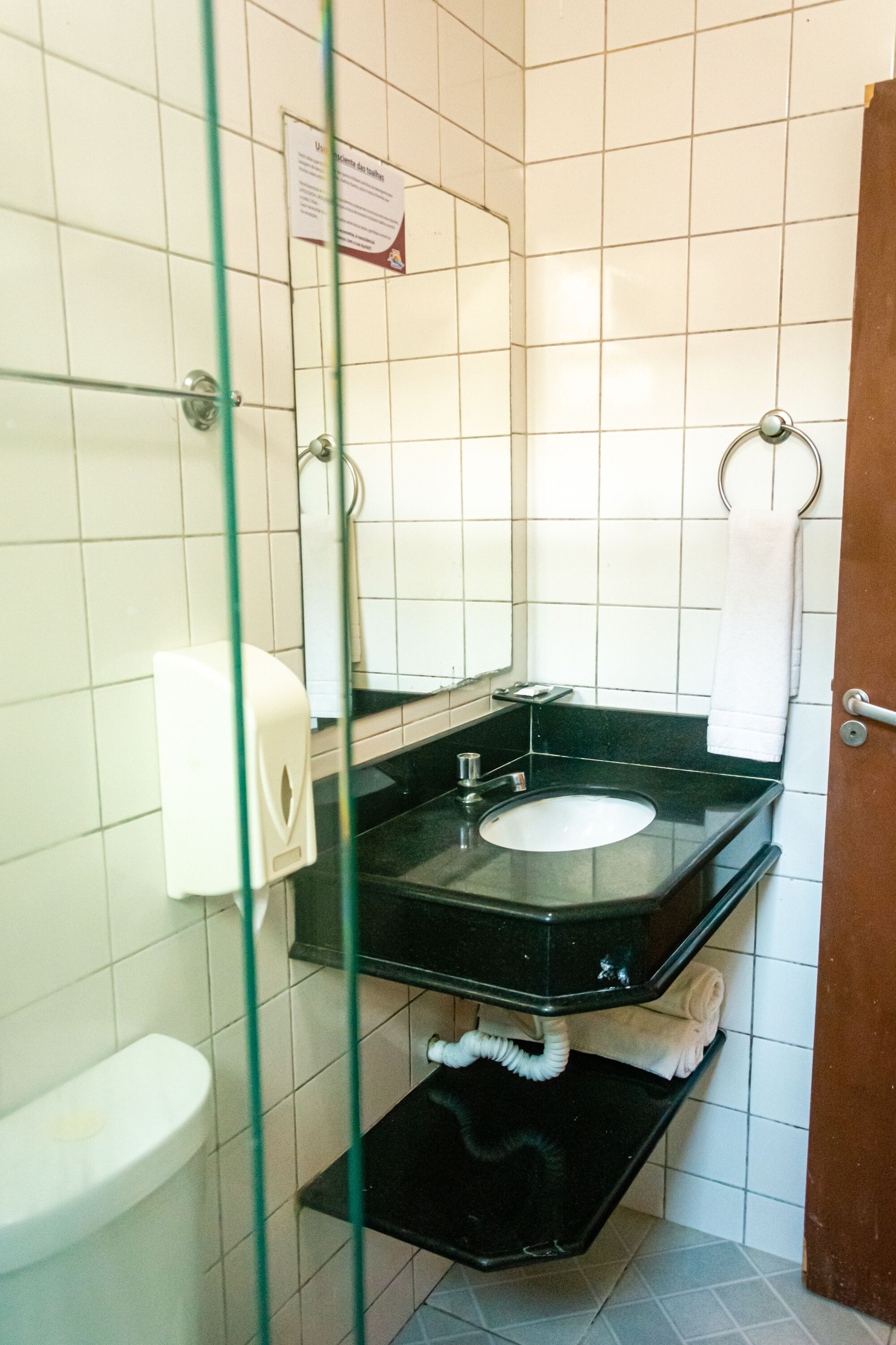 Un baño con inodoro blanco, lavamanos negro, espejo y perchero para toallas.