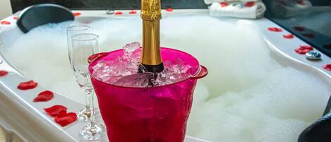 A bathtub with a champagne bottle, ice, and rose petals.