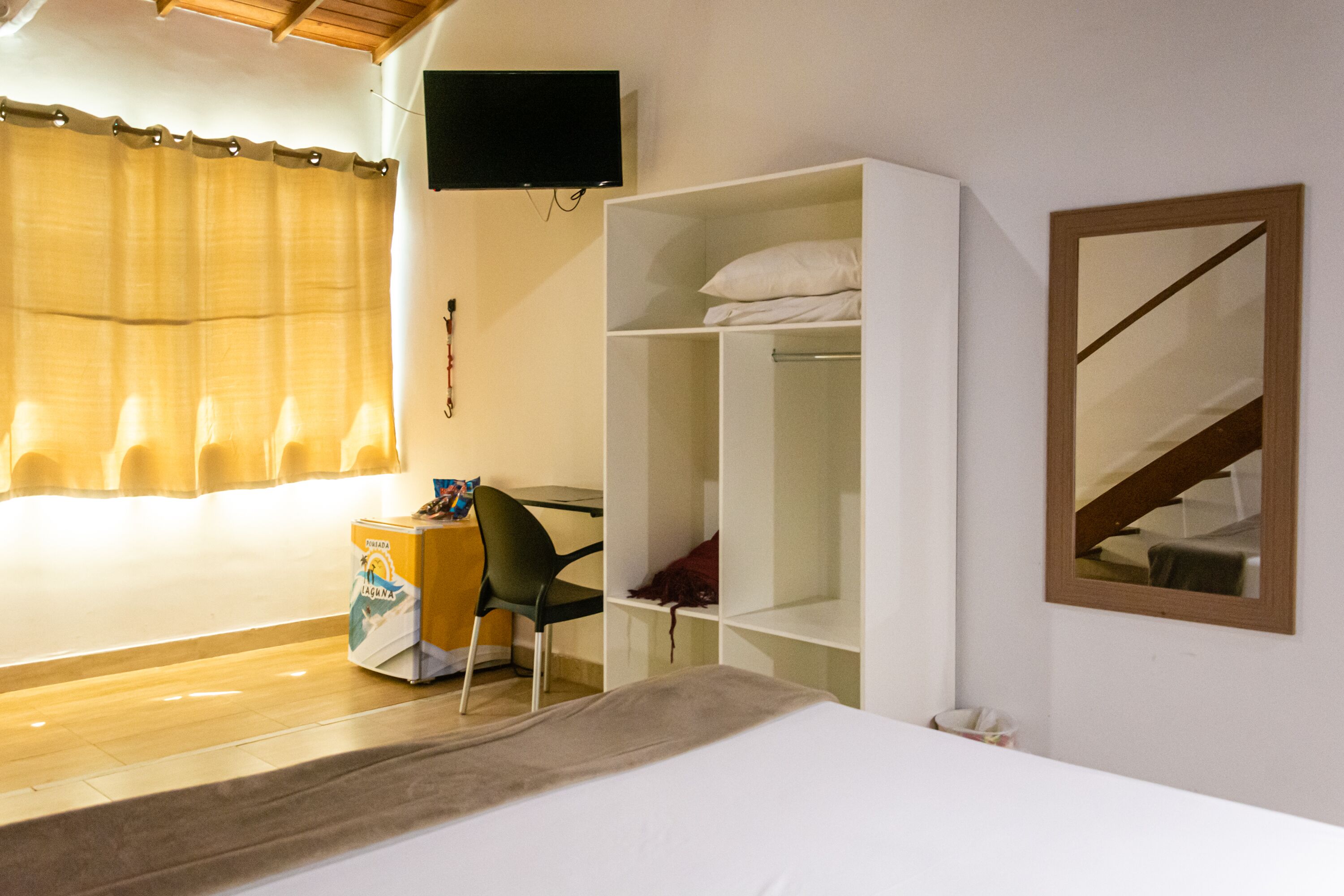 A hotel room with a bed, a desk with a chair, a wardrobe, a television, and a mirror.
