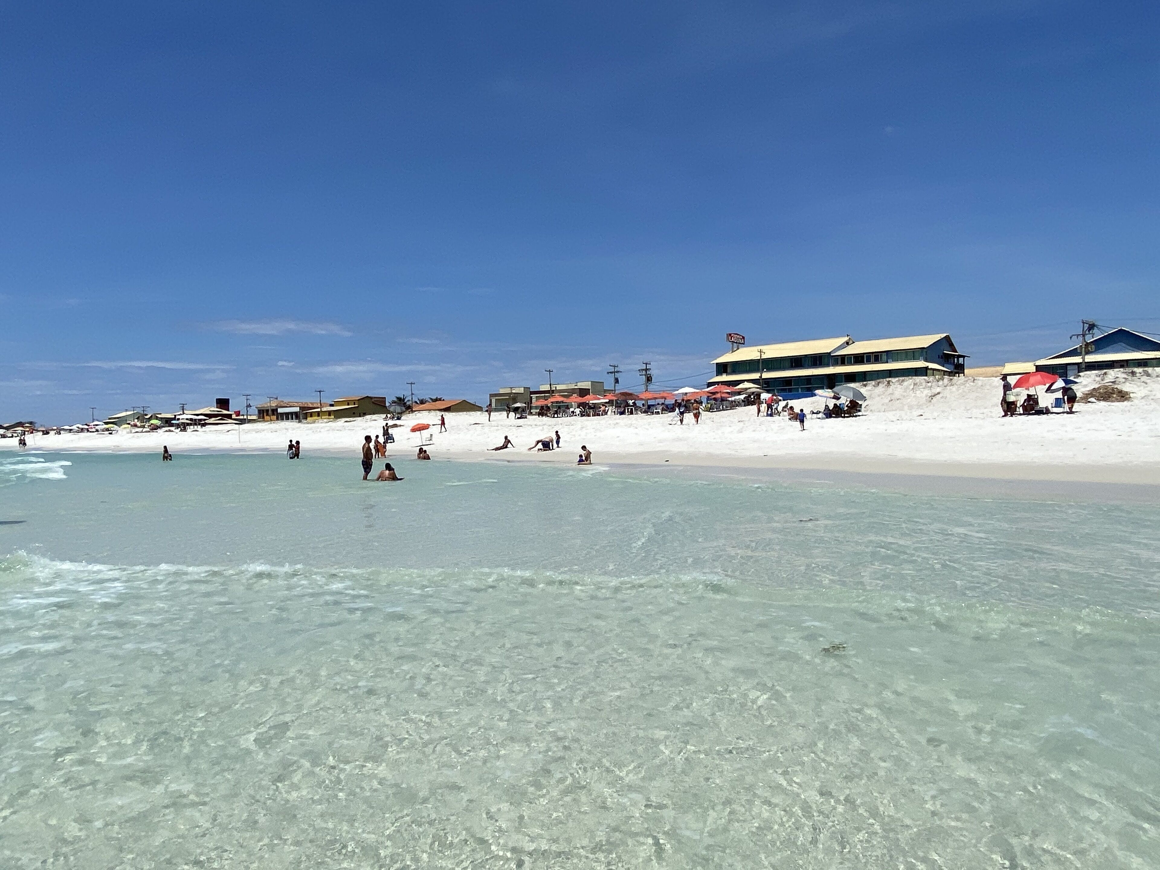 Una playa con agua cristalina, gente tomando el sol y edificios al fondo.