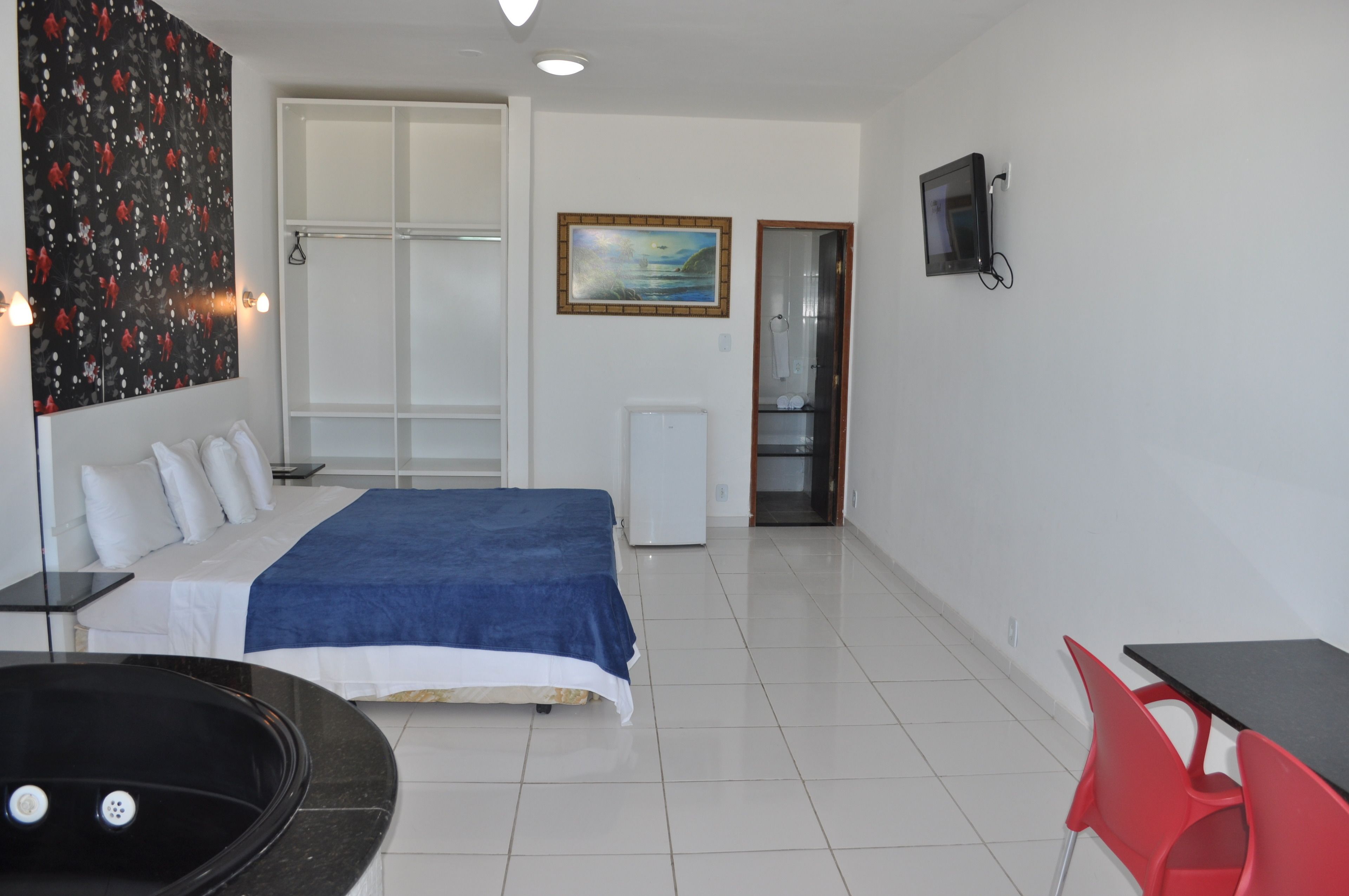 A hotel room with a bed, a desk, a chair, a TV, and a painting on the wall.