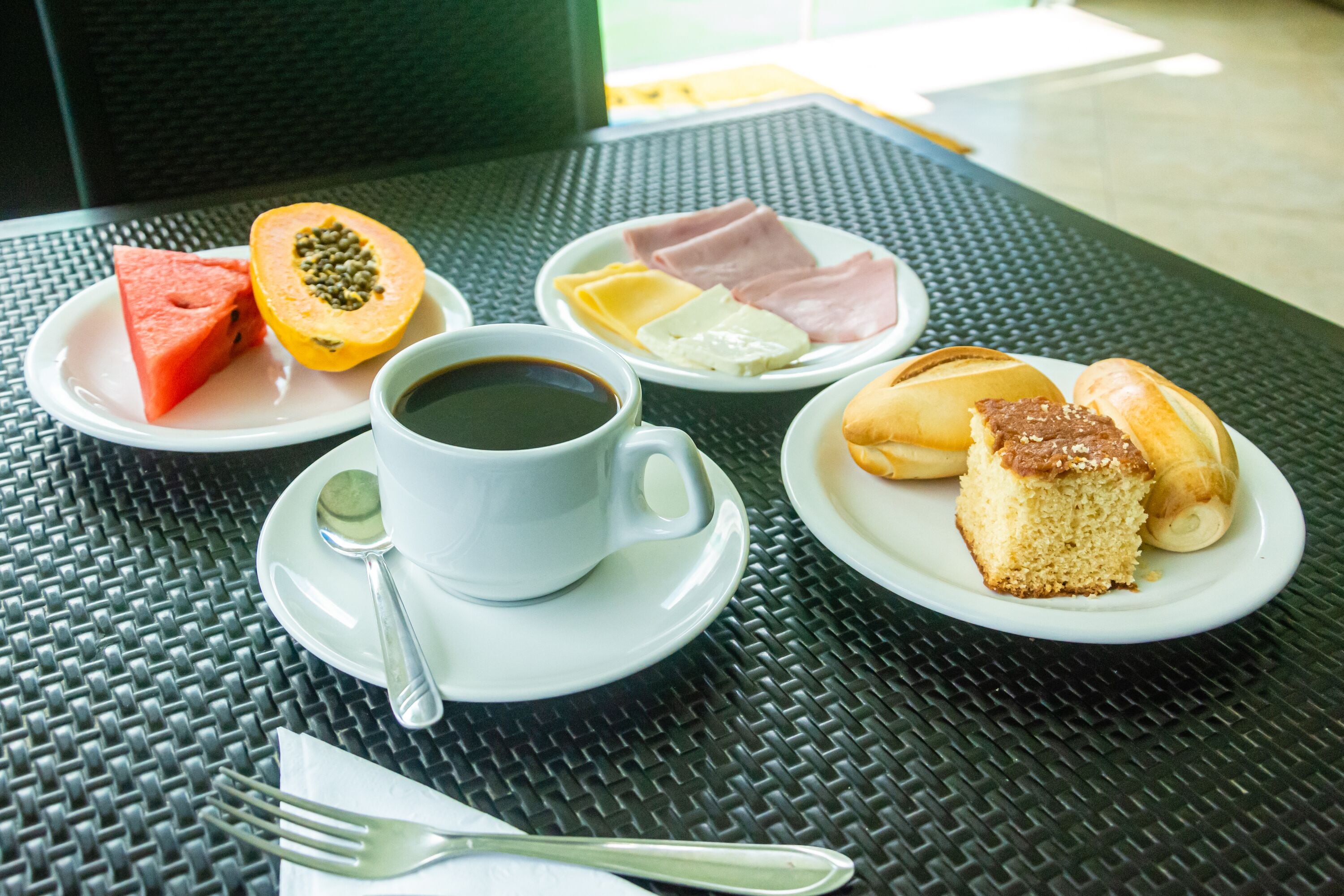 Et bord med en tallerken mad, blandt andet vandmelon, papaya, skinke, ost og brød, samt en kop kaffe.
