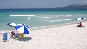 A beach with white sand, clear turquoise water, and a few umbrellas providing shade. - Pousada Laguna (Cabo Frio)