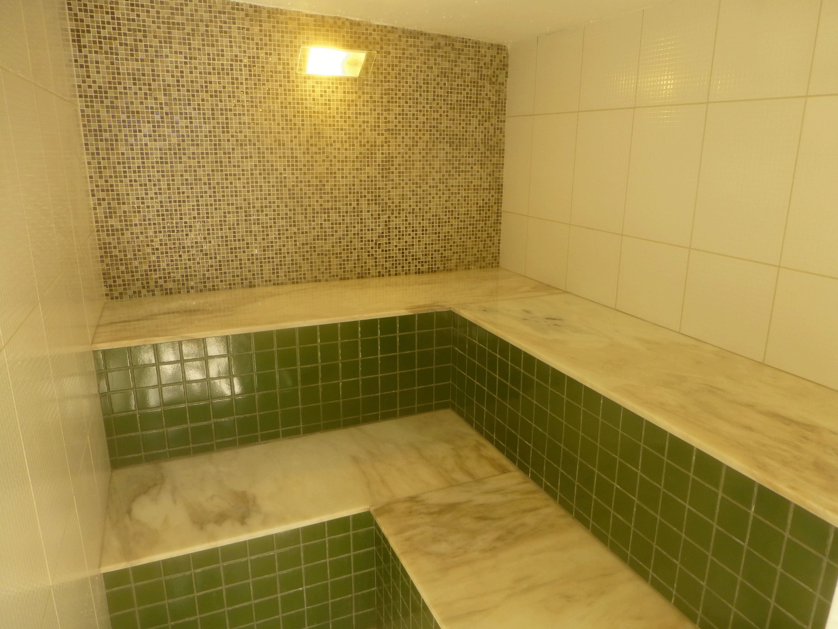 A bathroom with green and beige tiles, a white countertop, and a small window with a light fixture.