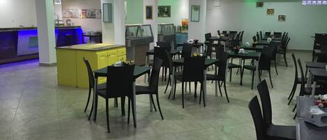 A restaurant with multiple tables and chairs, a kitchen area, and a bar.