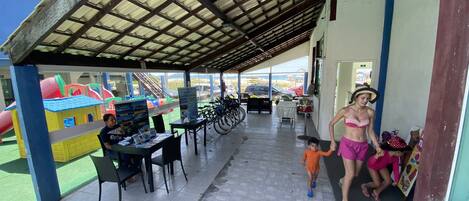 An outdoor covered area with a play structure, tables, chairs, and bicycles.