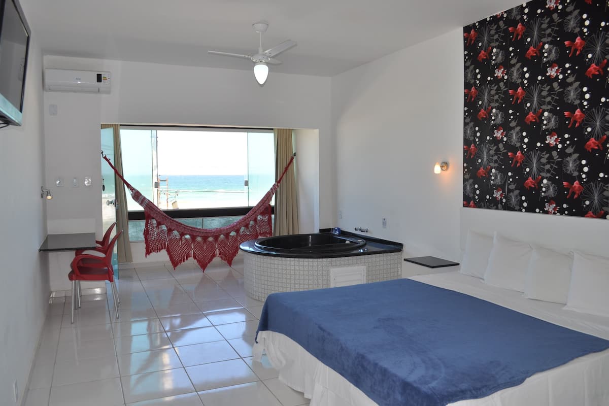 Ein Hotelzimmer mit Bett, einem roten Sessel, einem kleinen Tisch, einer Whirlwanne und Blick auf den Strand.