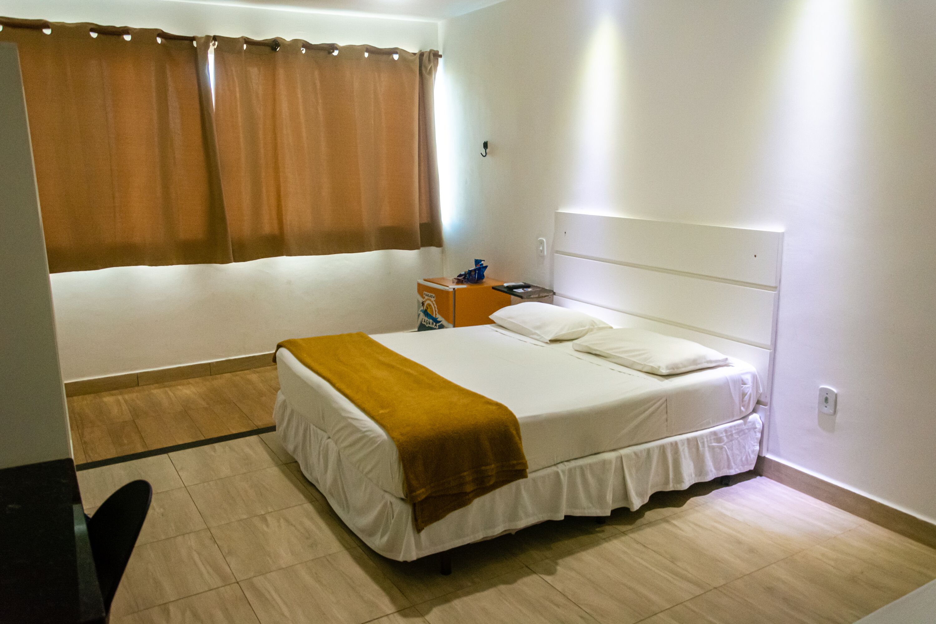 A hotel room with a single bed, a nightstand, a lamp, and a window with curtains.
