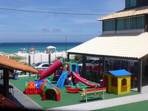 Un parque infantil con toboganes y estructuras para escalar, una playa al fondo y un edificio con tejado de baldosas.