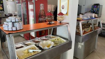 Un área de bufé con diversos alimentos, un refrigerador de Coca-Cola y una máquina de café.