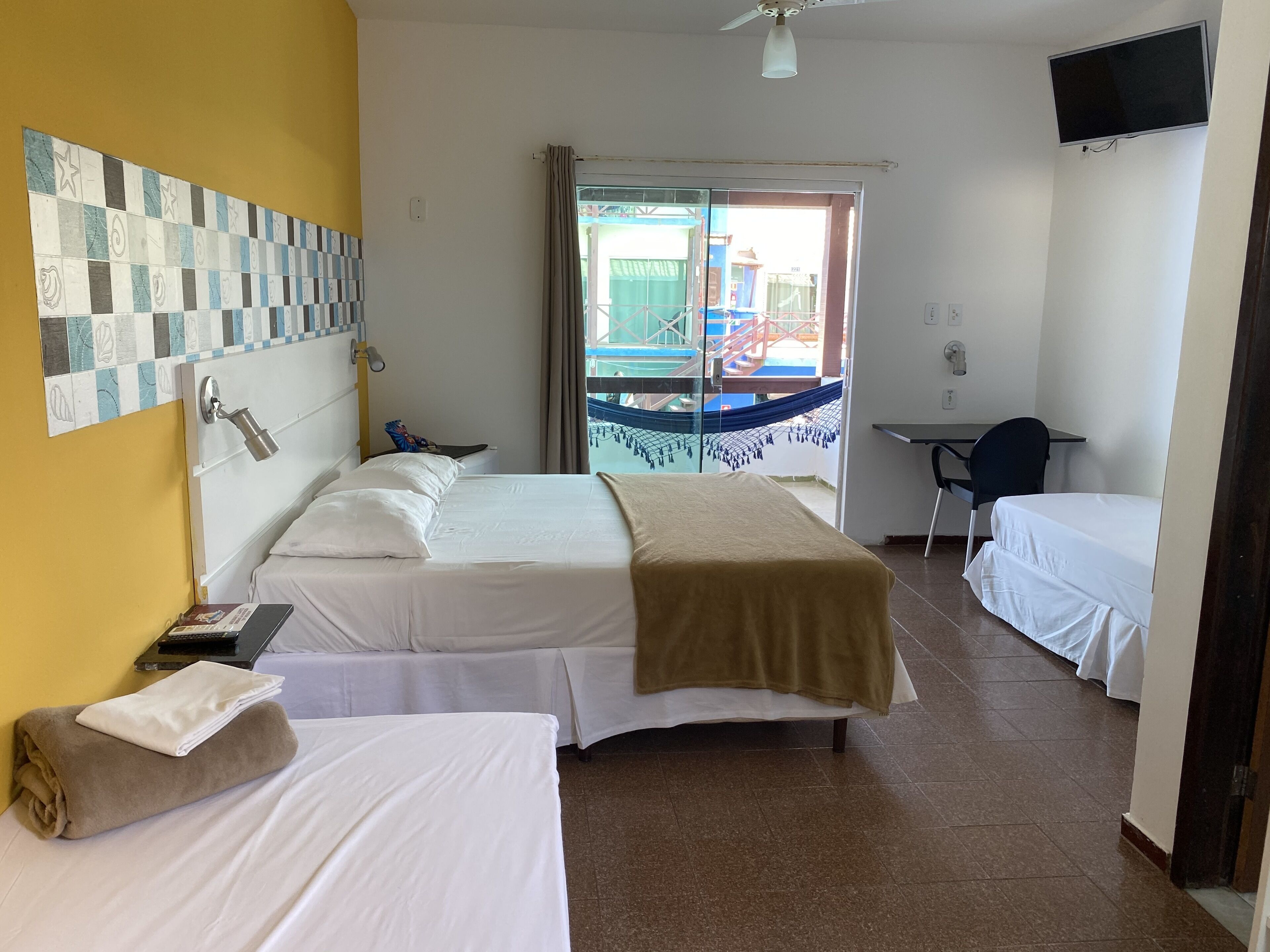 A hotel room with two beds, a desk, a TV, and a window with a view of a playground.