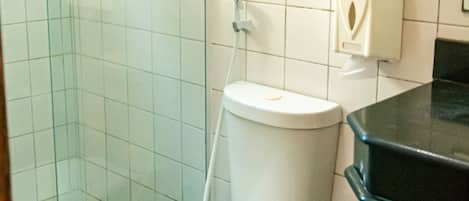 Egy fürdőszoba, amelyben található egy WC, egy üvegbetéttel ellátott zuhanyzó, egy adagoló a szappanhoz és egy szemeteskosár.