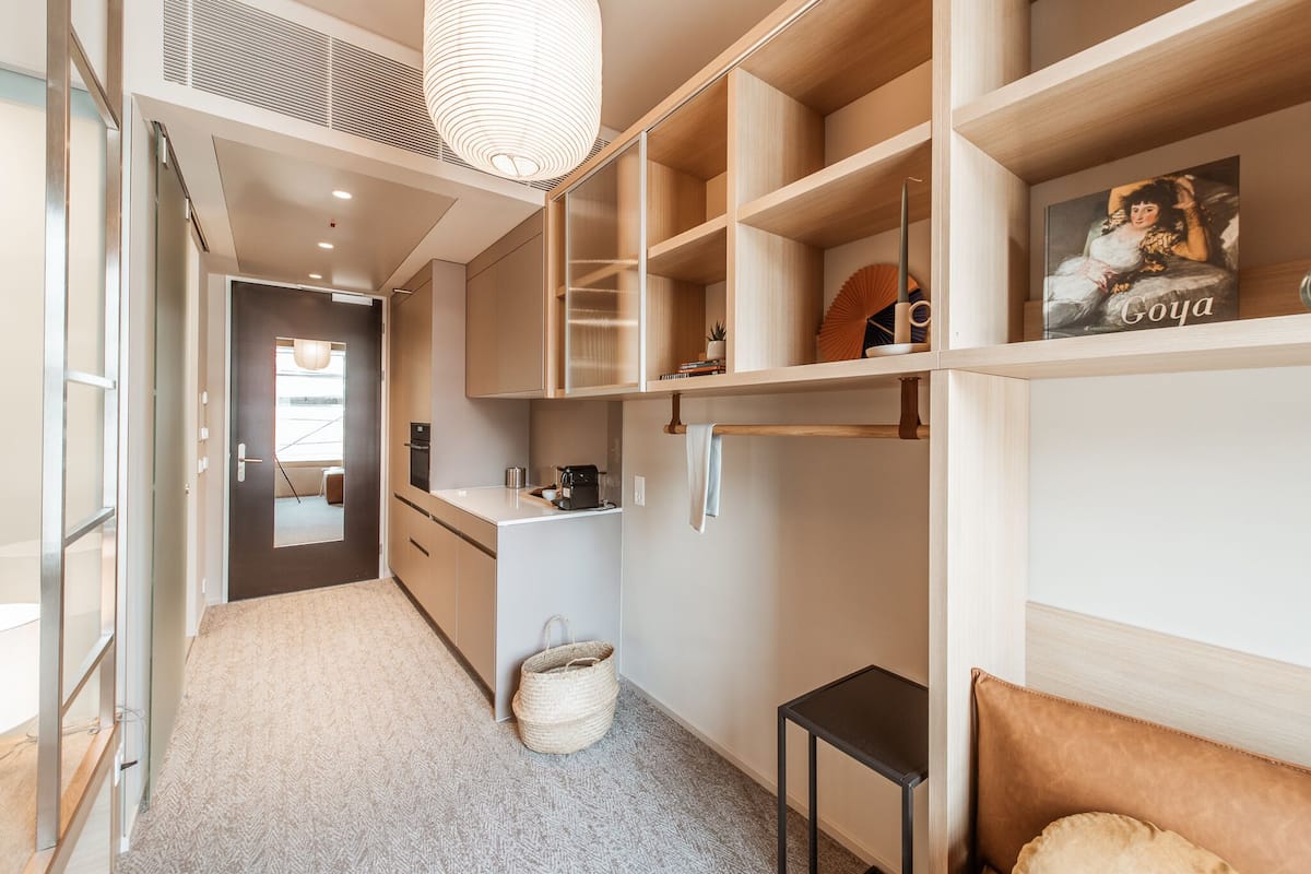 A modern, well-organized room with built-in shelving, a small kitchen area, and a cozy seating area.