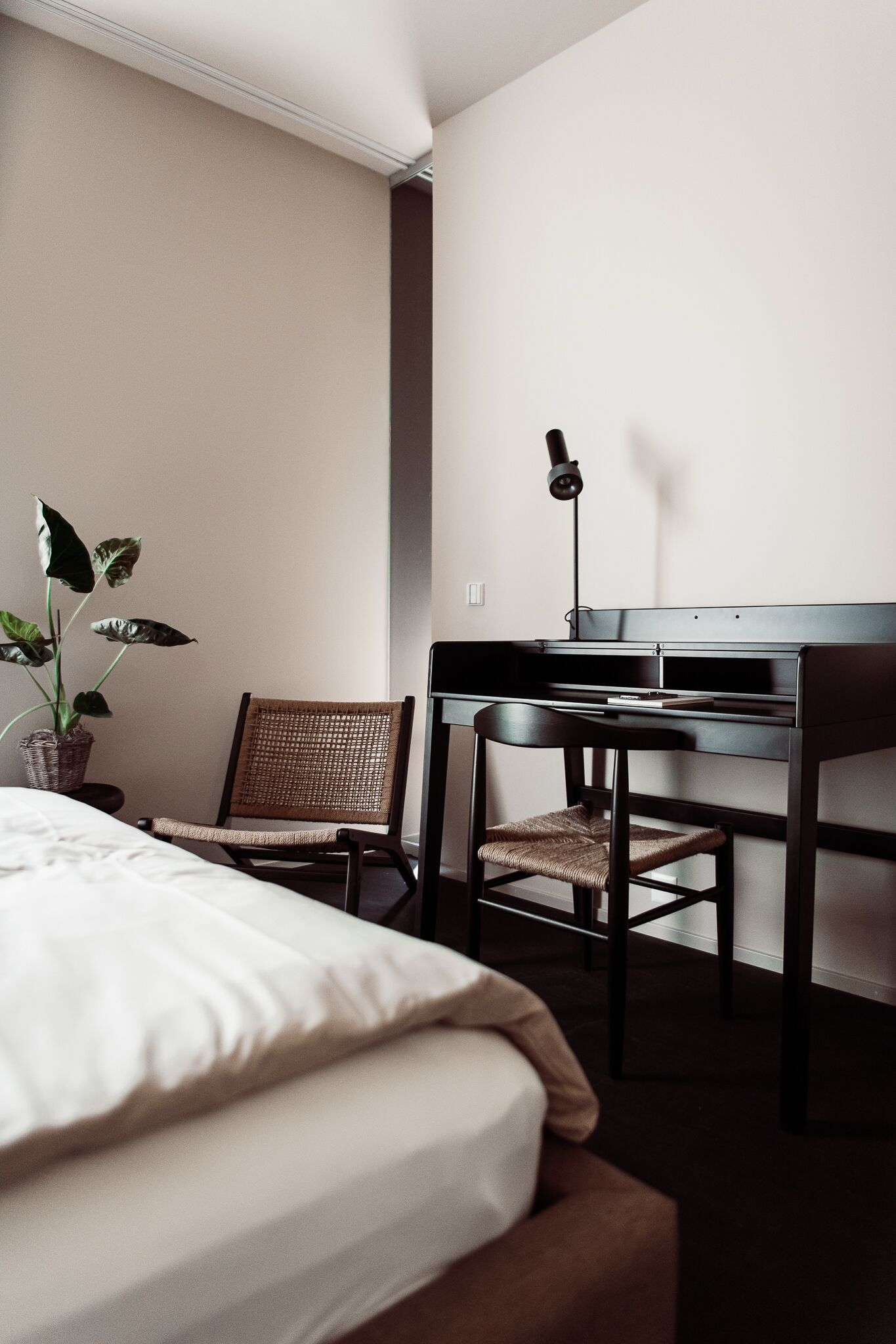 A hotel room with a bed, a desk, a chair, and a potted plant.