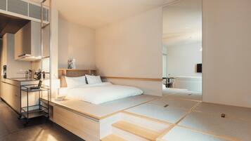 Une chambre d’hôtel moderne équipée d’un lit, d’une table de chevet, d’un miroir et d’un coin cuisine.