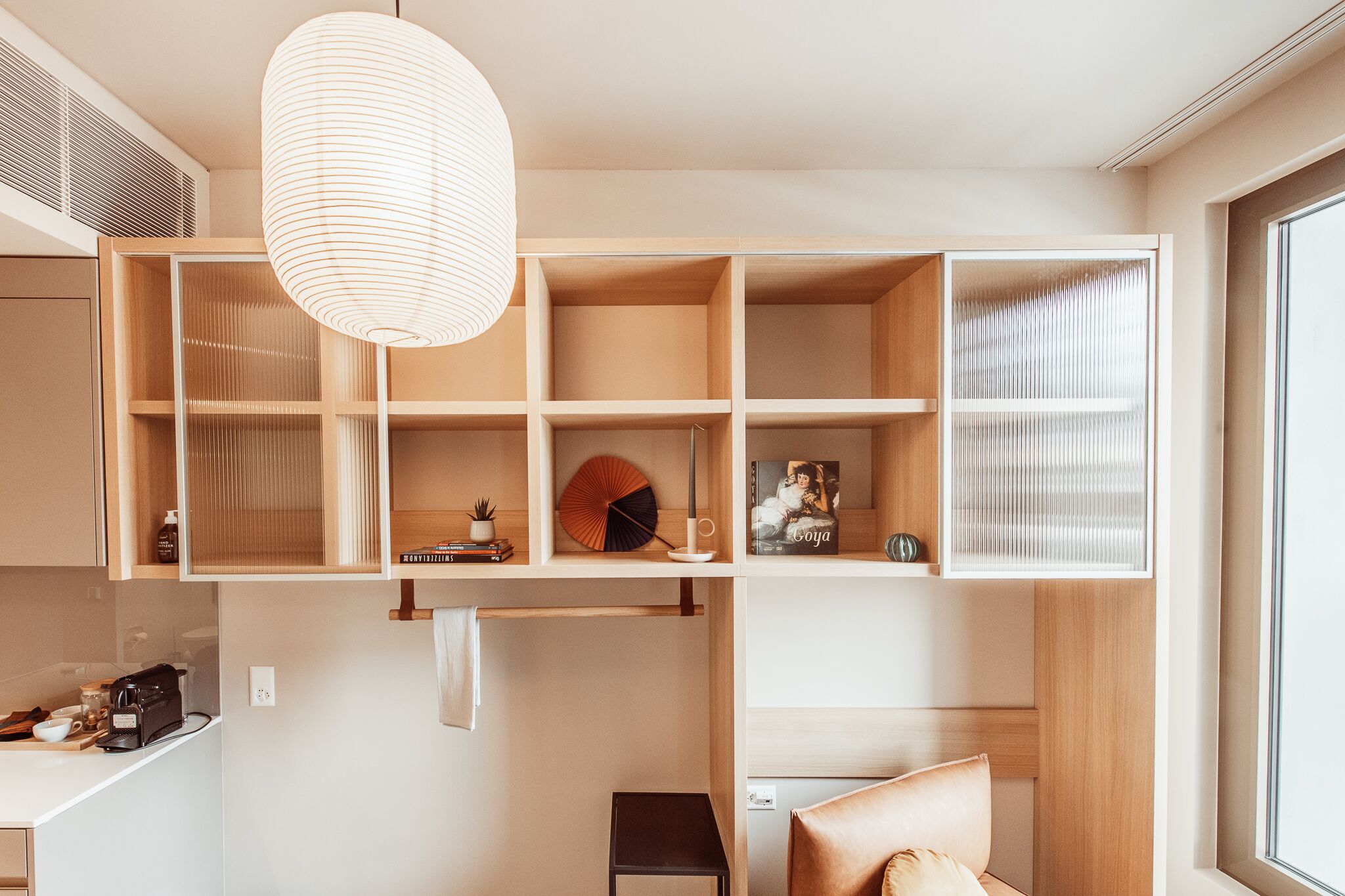 A modern interior with a built-in wooden shelving unit, a hanging light fixture, and a small table with a coffee maker.