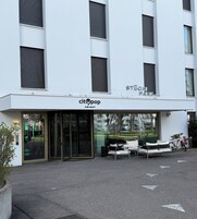 Un edificio moderno con entrada de vidrio, mesas al aire libre y bicicletas estacionadas afuera.