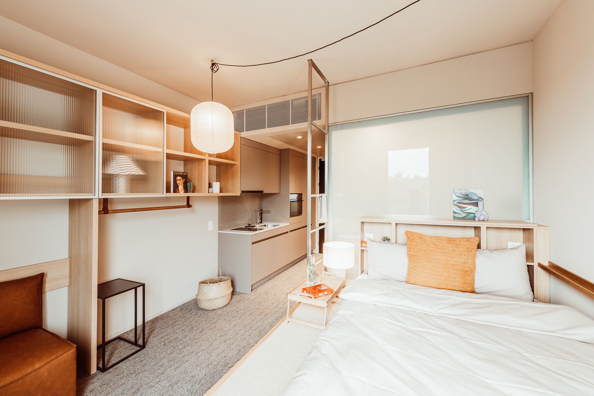 Una habitación de hotel moderna con una cama, mesita de noche, lámpara y vistas de la ciudad.