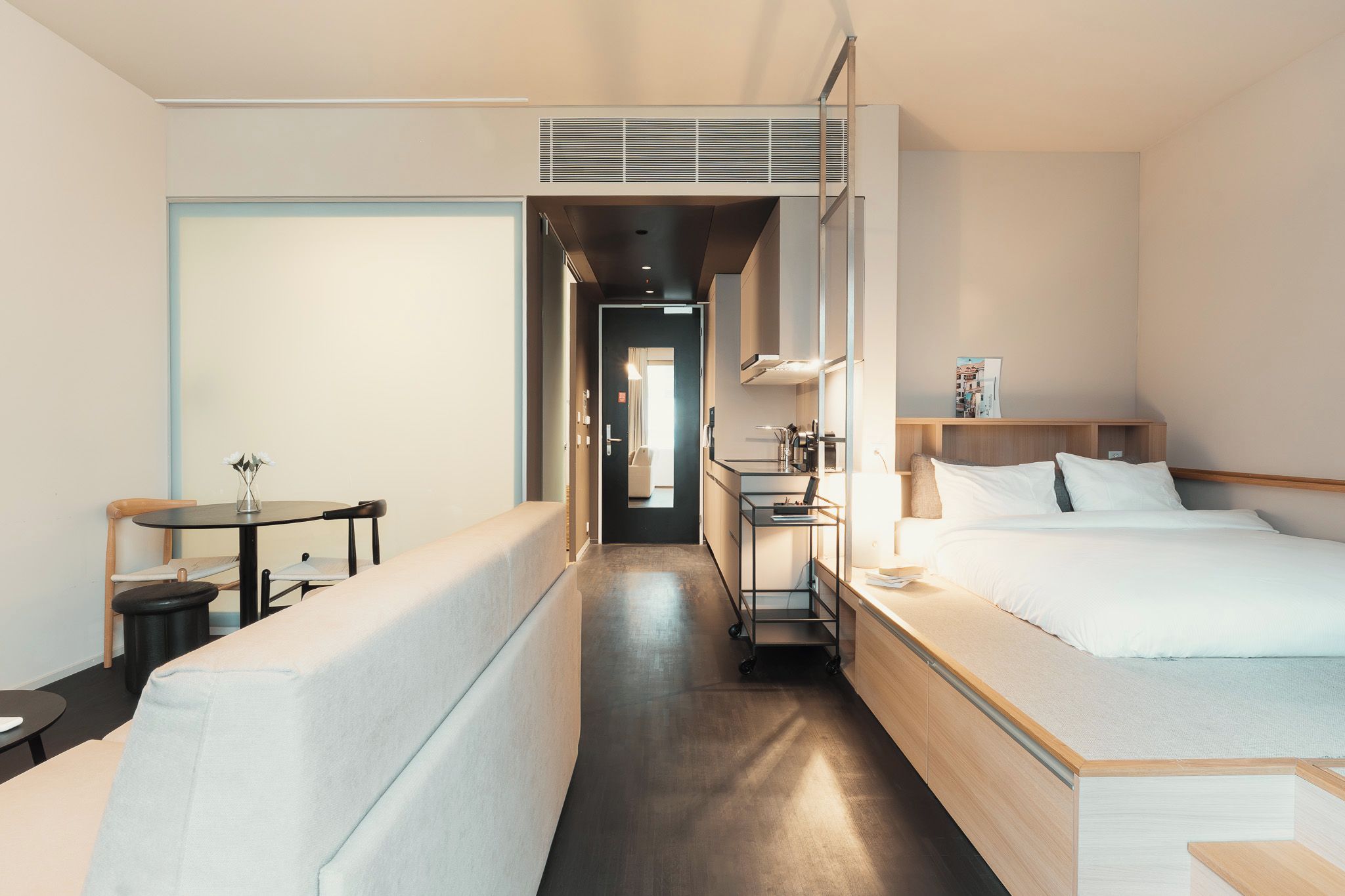 A hotel room with a bed, a desk, a chair, and a small table with a vase of flowers.