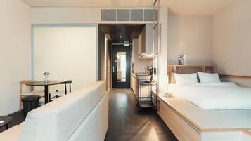 A hotel room with a bed, a desk, a chair, and a small table with a vase of flowers.