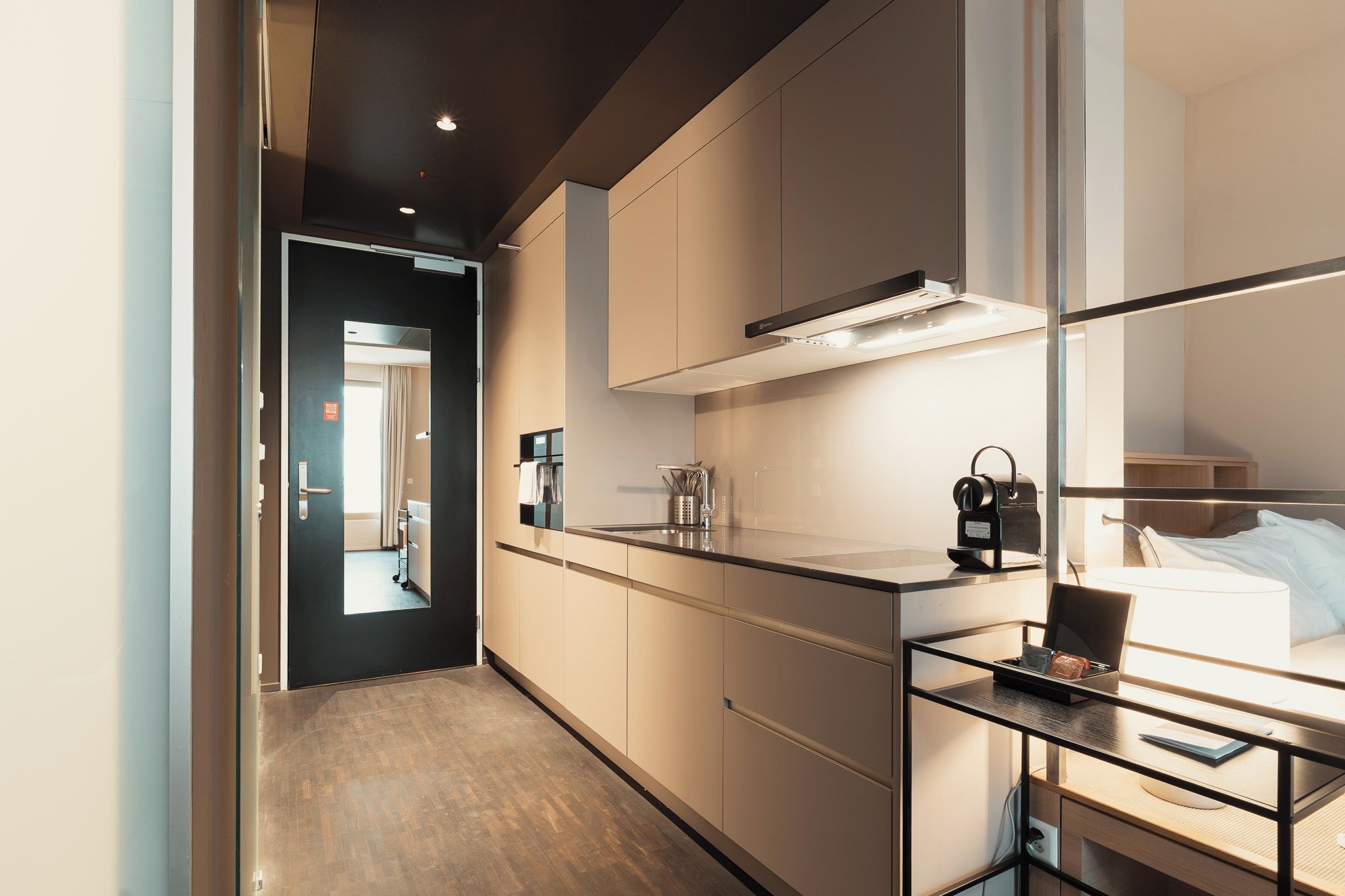 A modern hotel room with a kitchenette, a bed, and a desk area.