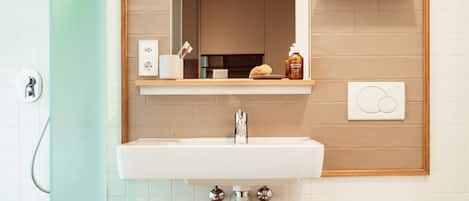 A modern bathroom with a white sink, a mirror, a toilet, and a shower.