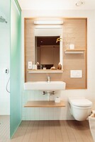 Un baño moderno con un lavabo blanco, un espejo, un inodoro y una ducha.