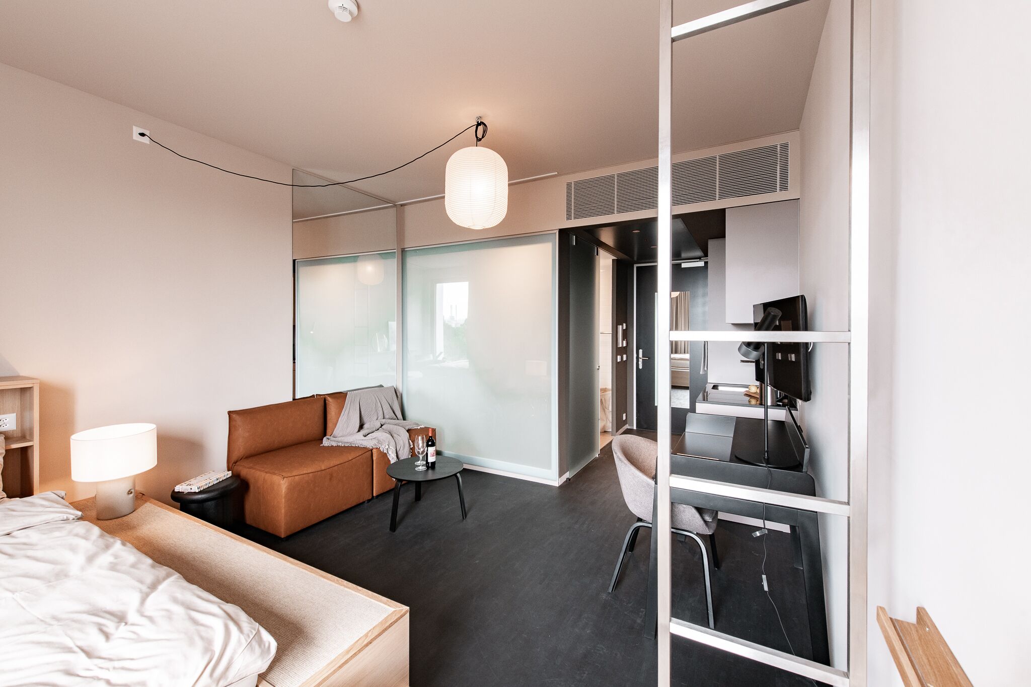 Ein modernes Hotelzimmer mit Bett, Sofa, Schreibtisch mit Computer und Stuhl.